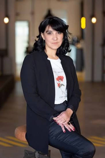 Gabriela Oliván sentada, con un blazer negro, en un corredor luminoso